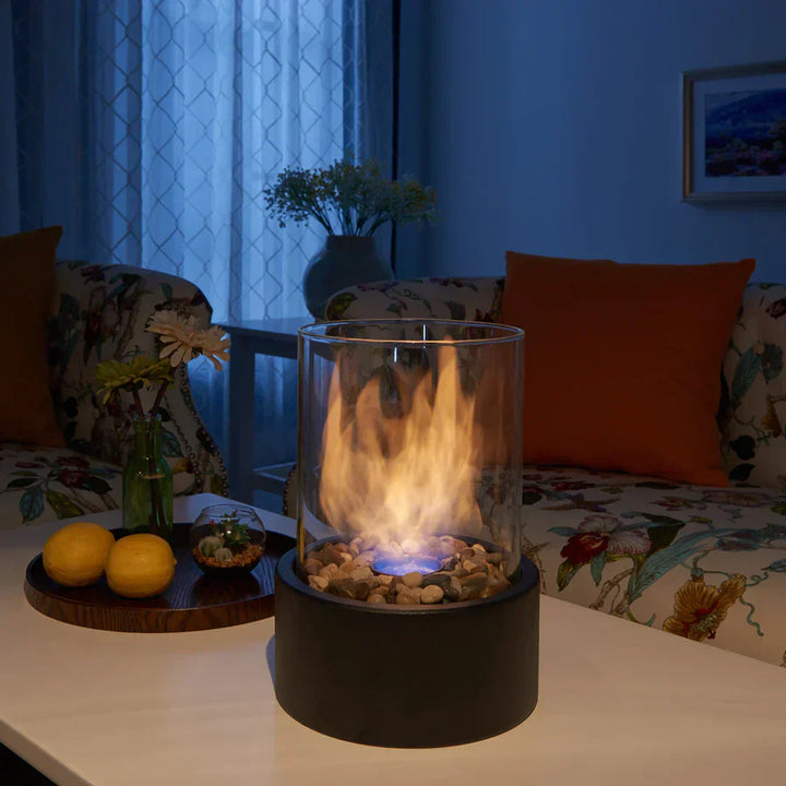 Cheminée portable moderne, design épuré, verre cylindrique, base métal noir. Ambiance chaleureuse.