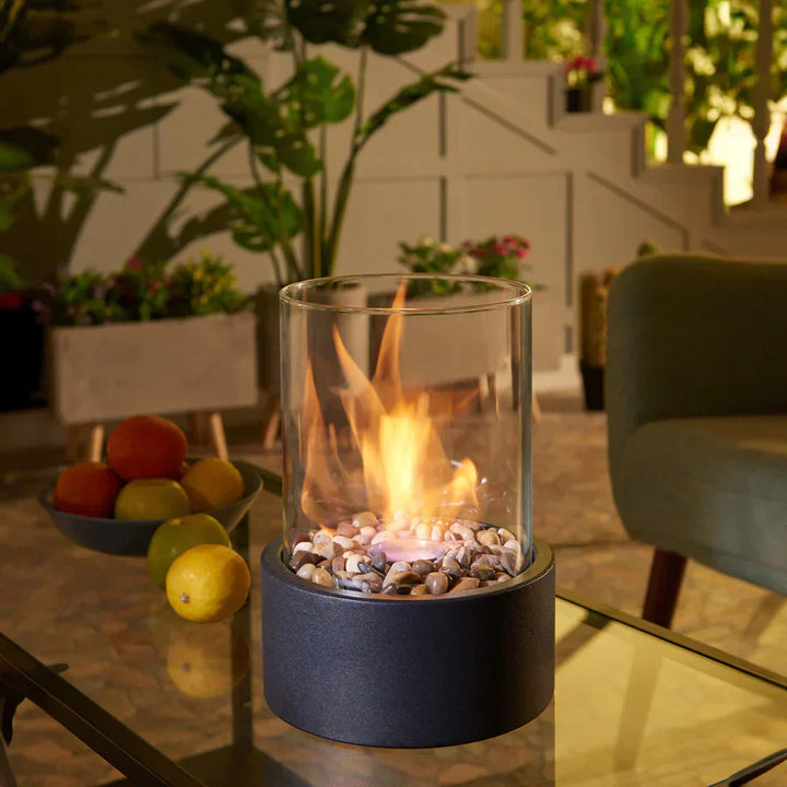 Cheminée portable moderne, design épuré, verre cylindrique, base métal noir. Ambiance chaleureuse.