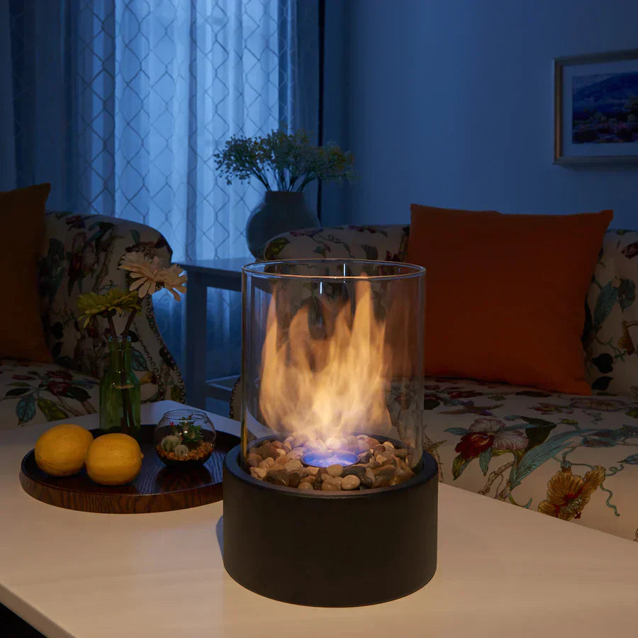 Cheminée portable moderne, design épuré, verre cylindrique, base métal noir. Ambiance chaleureuse.