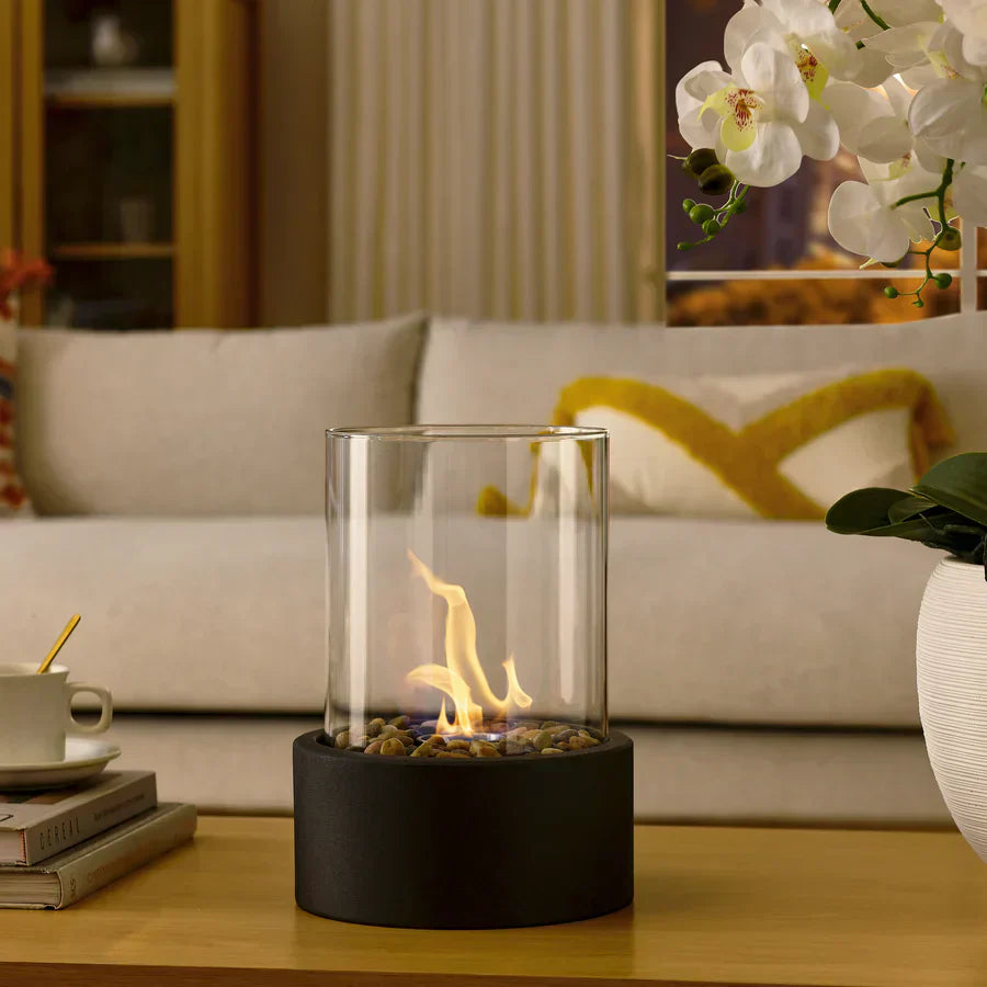 Cheminée portable moderne, design épuré, verre cylindrique, base métal noir. Ambiance chaleureuse.