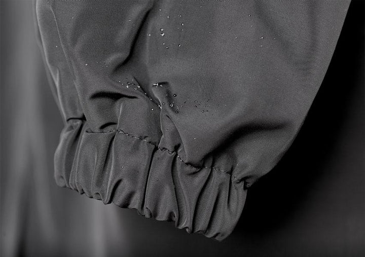 Silhouette d'une femme portant un manteau imperméable noir et sa capuche oversize, ambiance urbaine mystérieuse.