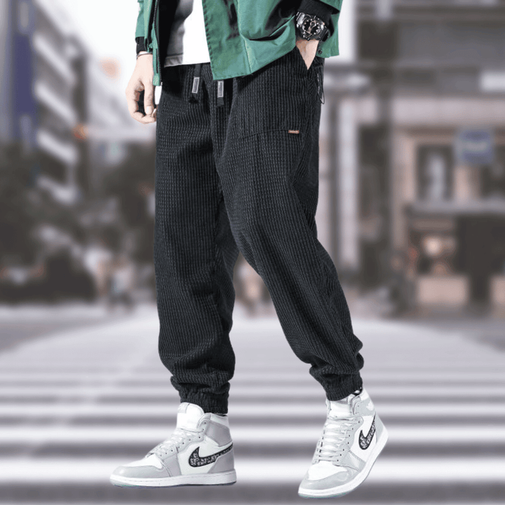 Pantalon noir homme chic en velours côtelé, style jogger décontracté et élégant.