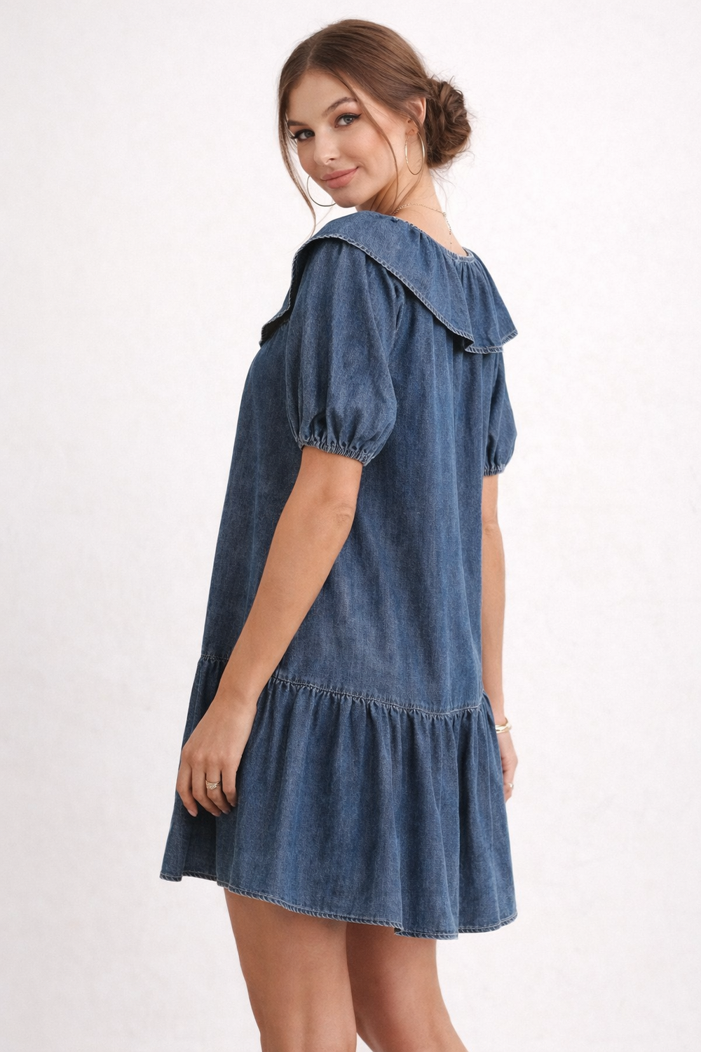 Femme portant une robe en jean courte et élégante avec manches bouffantes, look décontracté chic.
