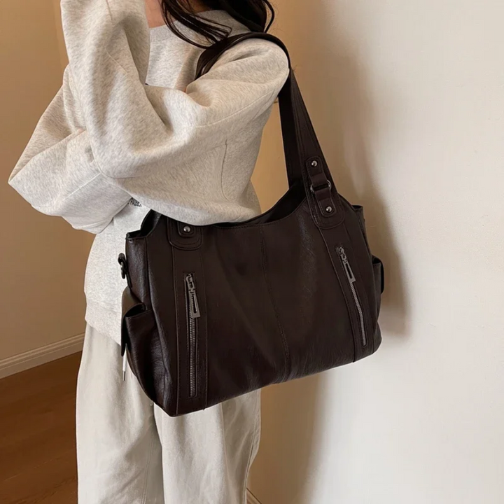 "Sac Amber en cuir végétal marron avec bandoulière, détails métalliques et poches, design élégant et spacieux pour femme."