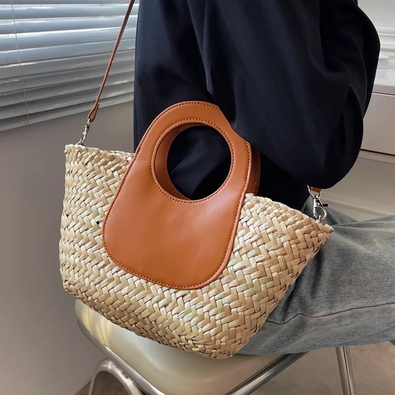 Gros plan d'un sac bandoulière femme estival, paille tressée et rabat en similicuir avec boucle dorée.