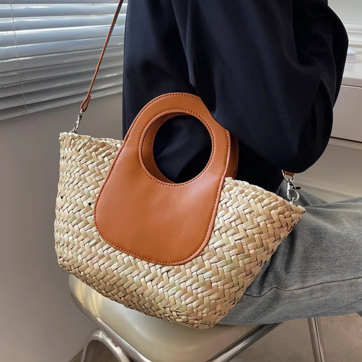 Gros plan d'un sac bandoulière femme estival, paille tressée et rabat en similicuir avec boucle dorée.