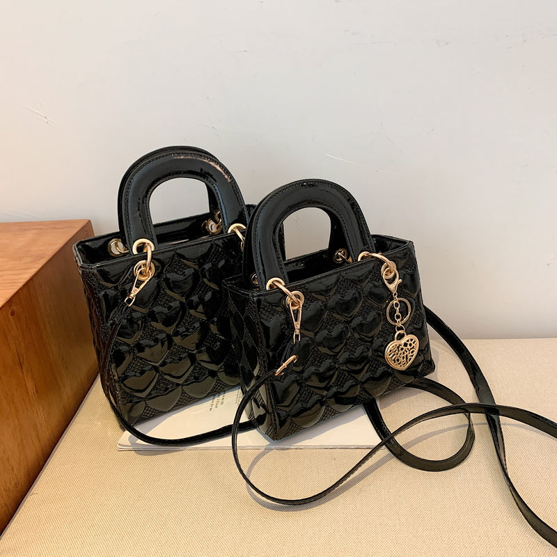 Sac femme noir brillant avec bandoulière, accessoire élégant et chic pour accompagner vos tenues de soirée.