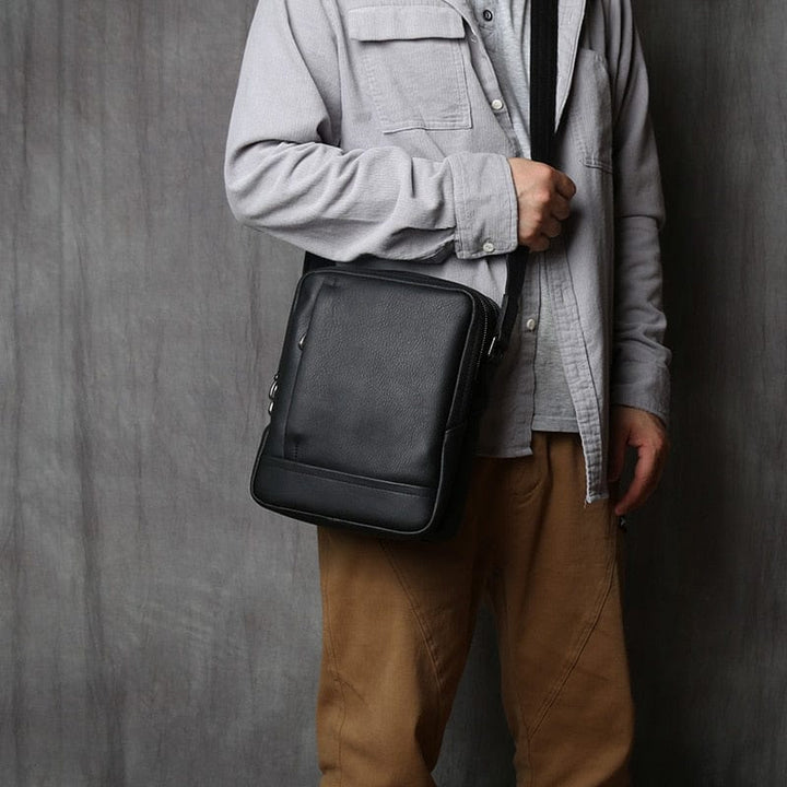 Sac bandoulière homme en cuir noir Aaron, plat, idéal pour transporter des essentiels au quotidien.