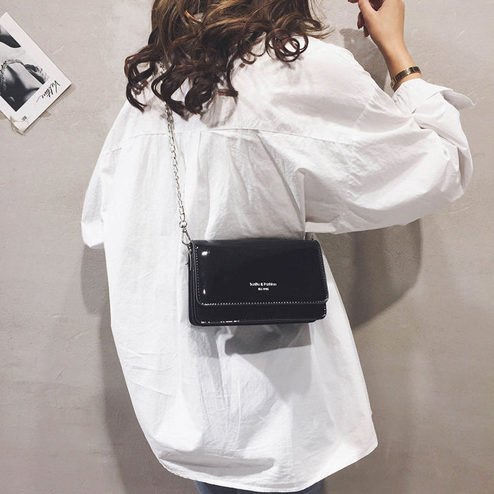 Sac à main noir vernis élégant pour femme, accessoire chic et compact pour toutes occasions.