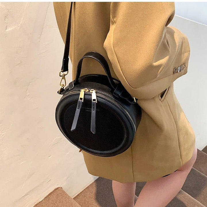 Sac rond noir chic en cuir synthétique, accessoire polyvalent pour femme. Fermeture dorée, forme unique.