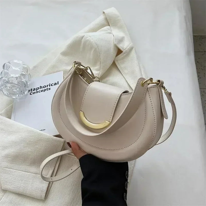 Sac rond élégant pour femme porté à l'épaule, montrant sa bandoulière fine et son design épuré.