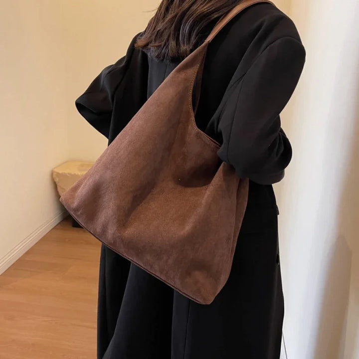 Femme portant sac besace en daim noir à l'épaule. Maroquinerie chic, look élégant et quotidien.