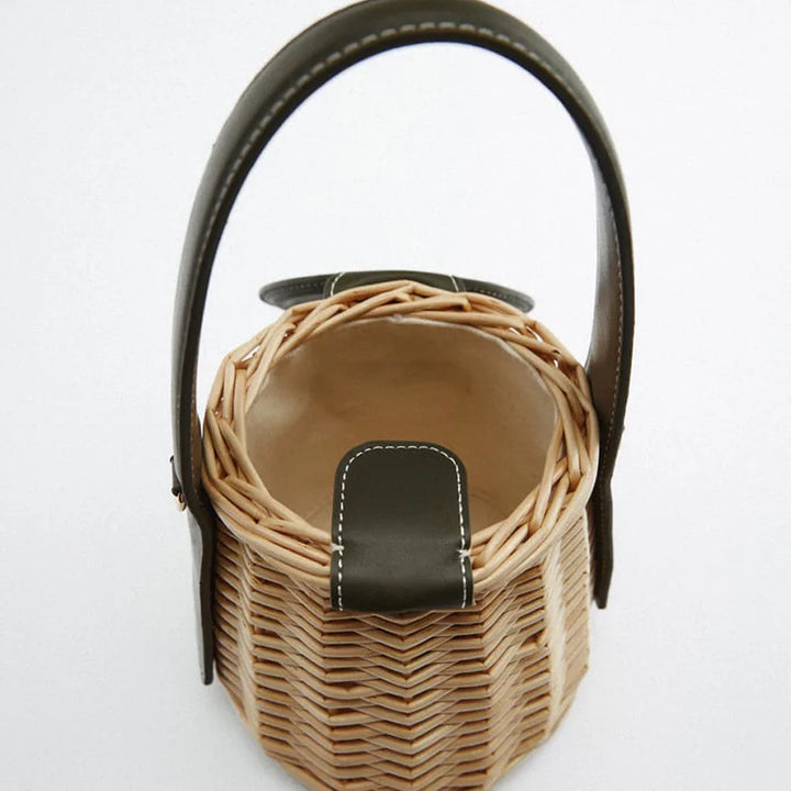 Accessoire femme: sac seau en paille tissée, muni d'une bandoulière et de détails en cuir vert foncé.