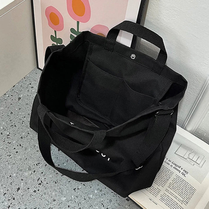 Sac cabas noir en toile de coton résistant, grand format, porté épaule, style intemporel et fonctionnel.