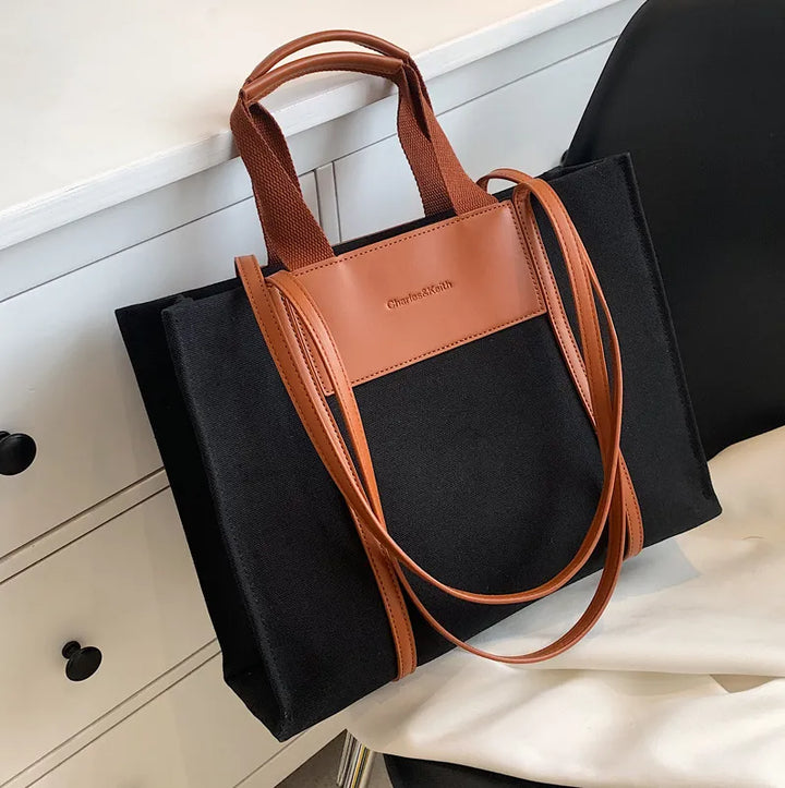 Femme portant un sac cabas à épaule en toile et similicuir noir, accessoire de mode pratique et chic pour la ville.