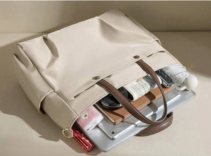 Sac de cours unisexe beige porté épaule, design fonctionnel et élégant, avec poches intérieures.