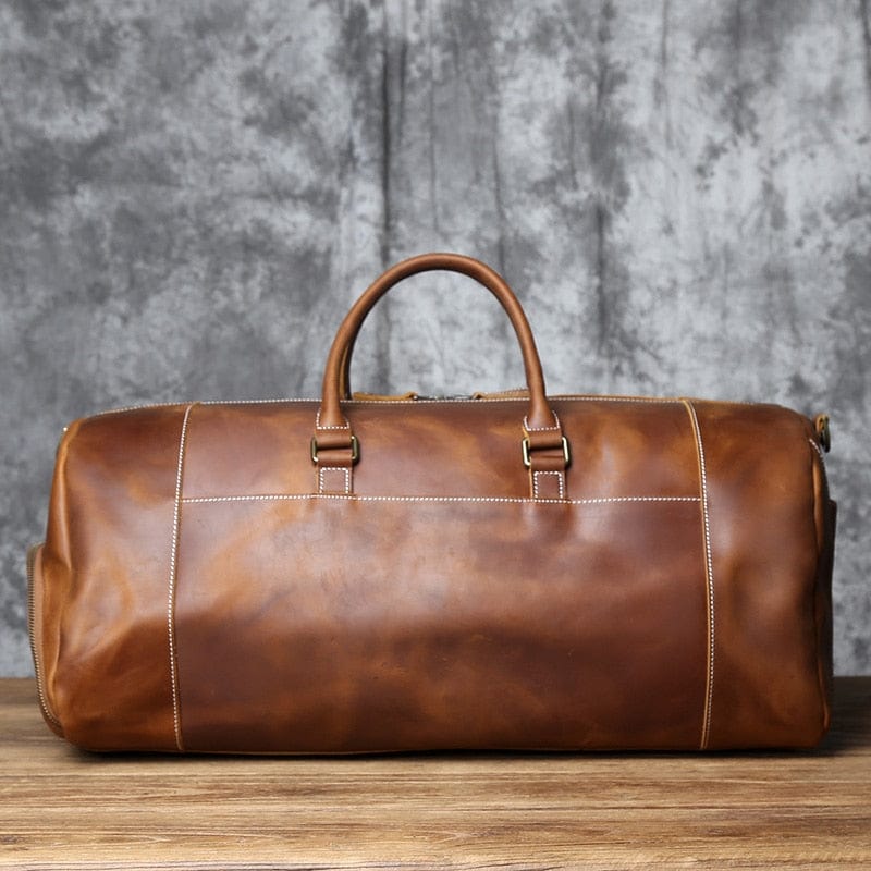 Sac de voyage en cuir homme avec étiquette bagage, détail des boucles métalliques, accessoire voyage.