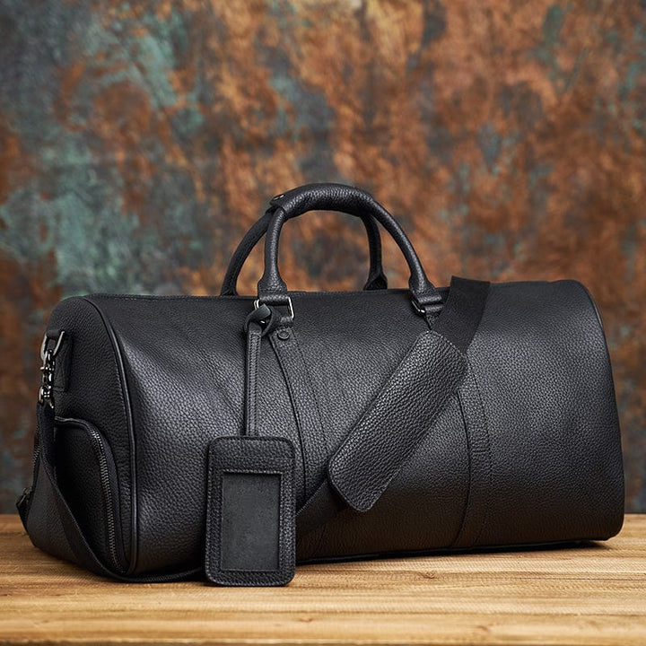 Sac de voyage homme en cuir foncé avec renforts en laiton, design intemporel et robuste.