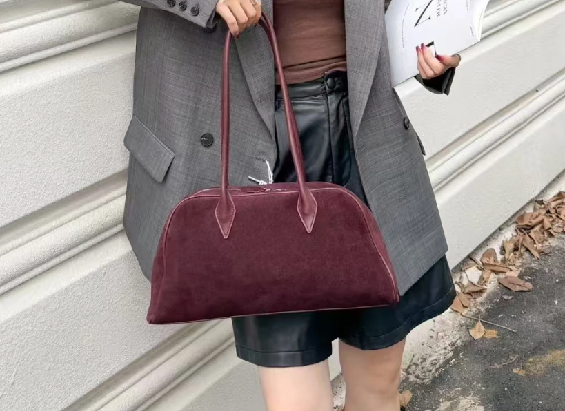 Gros plan sur la boucle décorative et la texture du daim d'un sac élégant pour femme, finition soignée.