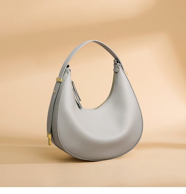 Femme portant un sac à main demi-lune en cuir véritable noir sur l'épaule, accessoire mode urbain et élégant.