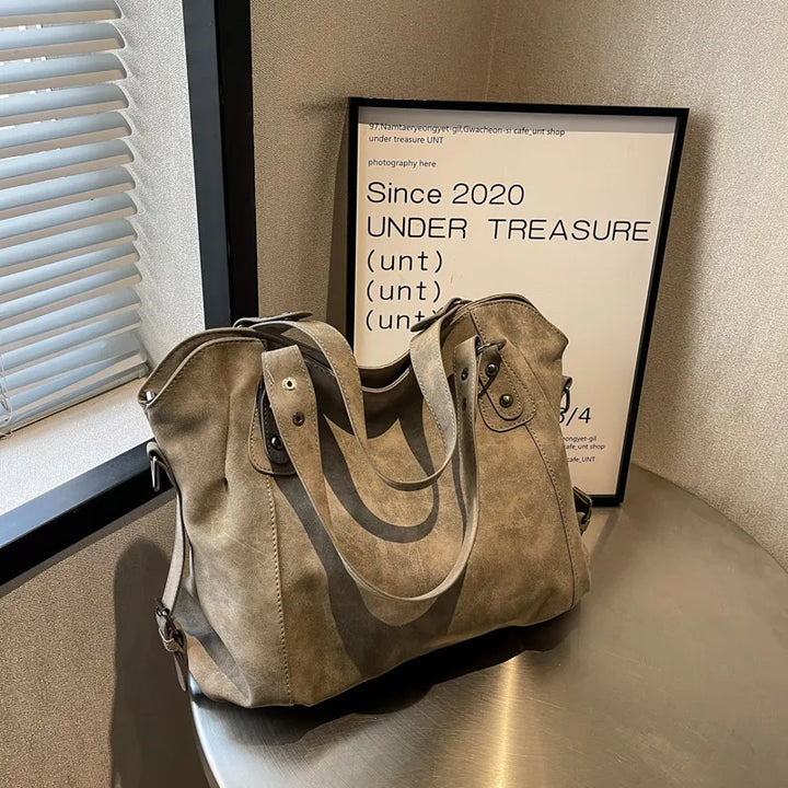 Vue détaillée du sac à main femme en daim, texture riche et boucles métalliques décoratives.