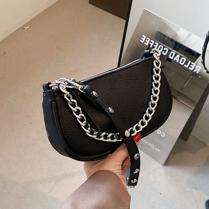 Sac à main femme noir élégant en cuir synthétique avec chaîne argentée, porté épaule, accessoire de mode tendance.