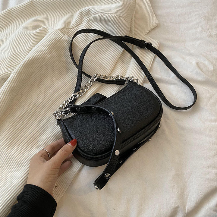 Sac à main noir pour femme avec bandoulière chaîne argentée, gros plan sur le détail du cuir et du fermoir.