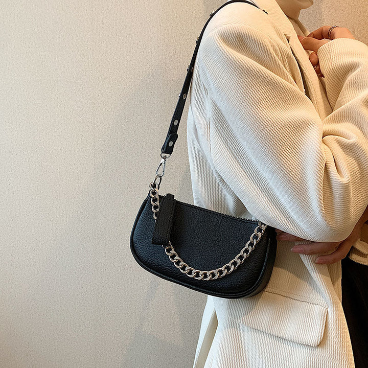 Accessoire de mode: Sac à main femme noir en cuir synthétique, avec anse chaîne argentée, positionné sur une table.