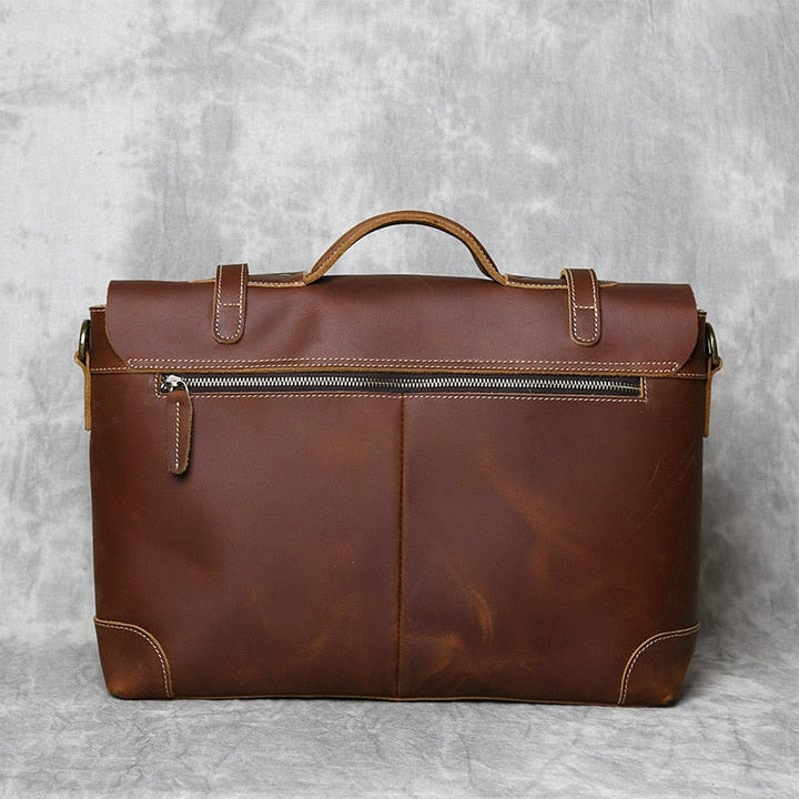 Gros plan sur la texture grainée du cuir d'un sac à main marron pour homme, soulignant sa qualité.