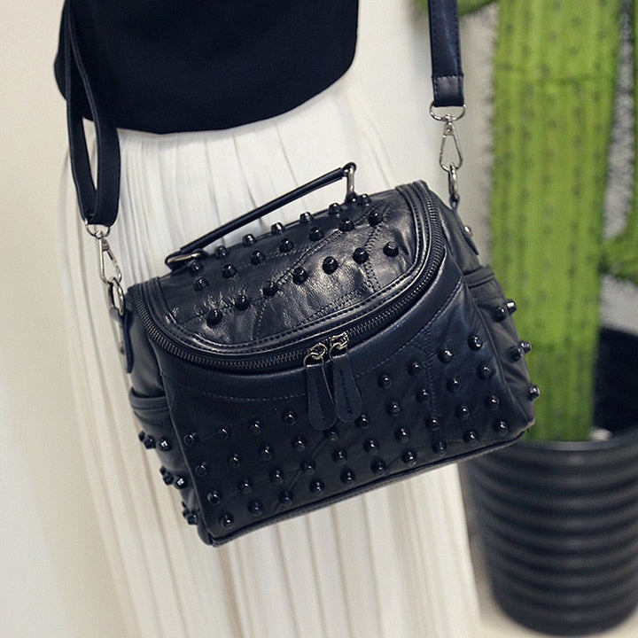 Élégant sac à main noir femme avec clous métalliques, bandoulière amovible.
