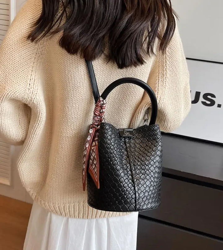 Sac seau en cuir vegan tressé posé sur une surface neutre, mettant en valeur sa couleur et sa forme.